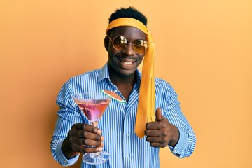 Wall Mural - Handsome black man drunk wearing tie over head and sunglasses drinking a cocktail smiling happy and positive, thumb up doing excellent and approval sign