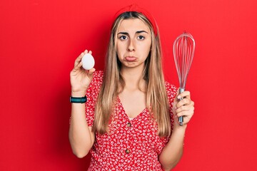 Poster - Beautiful hispanic woman holding egg and baker whisk depressed and worry for distress, crying angry and afraid. sad expression.