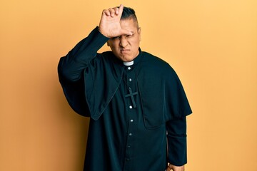 Canvas Print - Young latin priest man standing over yellow background making fun of people with fingers on forehead doing loser gesture mocking and insulting.