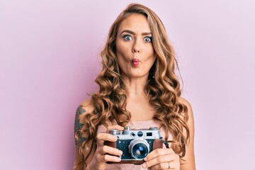 Poster - Young blonde girl holding vintage camera making fish face with mouth and squinting eyes, crazy and comical.