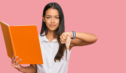 Canvas Print - Beautiful hispanic woman reading book with angry face, negative sign showing dislike with thumbs down, rejection concept