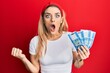 © Krakenimages.com - Young caucasian woman holding 1000 hungarian forint banknotes scared and amazed with open mouth for surprise, disbelief face