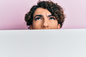 Young man wearing woman make up holding cardboard banner with blank space covering half face angry and mad screaming frustrated and furious, shouting with anger looking up.