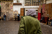 Street View, Downtown Damascus, Syria Featuring A Man From Behind Wearing A Palestinian Style Keffiyeh In The Old City Of Damascus, Syria. Cobblestone Streets And Other People Around Are Seen Blurred.