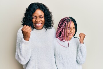 Sticker - Beautiful african american mother and daughter wearing casual winter sweater very happy and excited doing winner gesture with arms raised, smiling and screaming for success. celebration concept.