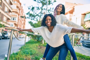 Sticker - Beautiful african american mother giving daughter piggyback ride with open arms at the park.