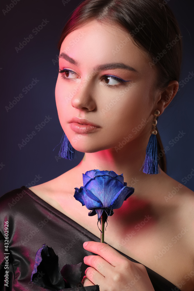 Beautiful young woman with blue rose on dark background