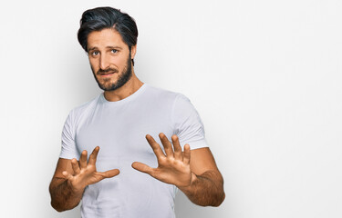 Young hispanic man wearing casual white t shirt disgusted expression, displeased and fearful doing disgust face because aversion reaction. with hands raised