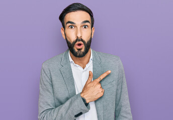 Wall Mural - Young hispanic man wearing business clothes surprised pointing with finger to the side, open mouth amazed expression.