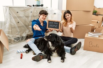 Poster - Young caucasian couple with dog holding our first home blackboard at new house smiling cheerful offering palm hand giving assistance and acceptance.