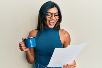 Wall Mural - Young latin transsexual transgender woman drinking cup of coffee and reading paper smiling and laughing hard out loud because funny crazy joke.