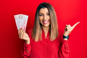 Poster - Beautiful brunette woman holding 500 swedish krona banknotes smiling happy pointing with hand and finger to the side