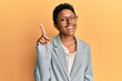 Young african american girl wearing business jacket and glasses showing and pointing up with finger number one while smiling confident and happy.