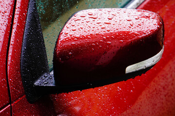 Water drops on the rear view mirror of a red car, after rain.