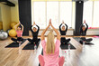 © zamuruev - Attractive female coach lead yoga class teach Caucasian group of people meditating together, girls raised arms up make Namaste gesture seated in lotus pose working out indoor