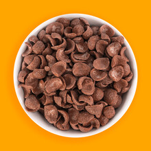 Top view of bowl with sweet chocolate cereal flakes for breakfast on yellow background