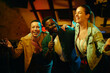 Cheerful African American man singing karaoke with female friends during a night out at the pub.
