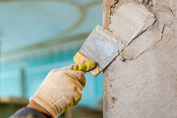 Wall Mural - Worker is cementing by the putty knife the wall in room that is under construction, remodeling, renovation, extension, restoration and reconstruction. Focus effect on the worker's hand.