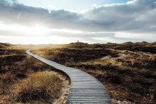 Wooden Footpath To Lighthouse Winding Among Heaps Of Coastal Sand Overgrown With Vegetation.