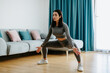 © shevtsovy - Young attractive woman practicing yoga at home in living room, stretching practice. Relaxation and meditation in living room. Beautiful fitness female wearing yoga pants gymnastics morning routine.