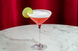cosmopolitan cocktail with lime and salted rim on marble table and red curtain behind