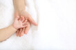 Baby little hand on mom's hand against white sheets background
