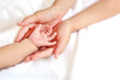 Mother's hand gently wrapping baby's hand on white sheets 