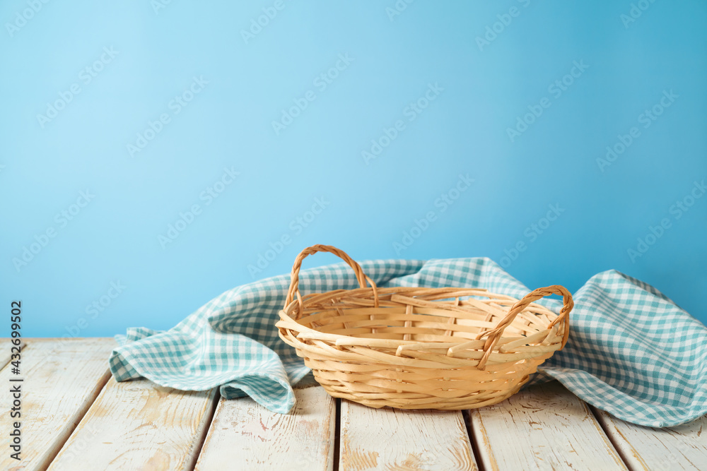 Empty wicker basket with tablecloth on rustic table over blue wall  background.  Kitchen mock up for design and product display. - obrazy, fototapety, plakaty 