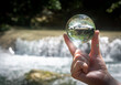 Closeup of a female hand holding a crystal glass ball displaying a waterfall in the forest. Concept of environment, nature protection, ecology. Tuscany, Italy