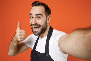 Wall Mural - Young confident man 20s barista bartender barman employee wearing black apron white t-shirt work in coffee shop show thumb up like gesture isolated on orange background studioSmall business startup.