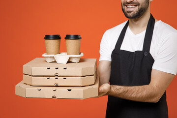 Wall Mural - Close up cropped photo portrait shot man barista bartender barman employee in apron tshirt work in coffee shop hold delivery cup pizza cardboard flatbox isolated on orange background Business startup