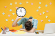 Young tired exhausted sad employee business man wearing shirt sit work white office desk with pc laptop hold clock putting hand on desk sleeping isolated on yellow color background studio portrait