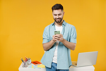 Wall Mural - Young smiling happy successful employee business man in shirt stand work at white office desk with laptop hold mobile cell chat online browsing surfing isolated on yellow background studio portrait