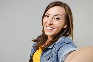 Poster - Close up young fun cheerful friendly smiling happy caucasian woman 20s wear casual denim jacket yellow t-shirt doing selfie shot on mobile phone look camera isolated on grey color background studio