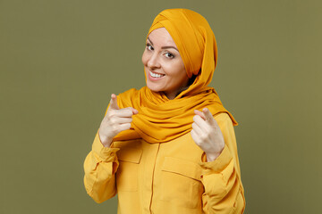 Wall Mural - Leader young arabian asian muslim woman in abaya hijab yellow clothes point index finger camera on you motivating isolated on olive green background. People uae middle eastern islam religious concept.