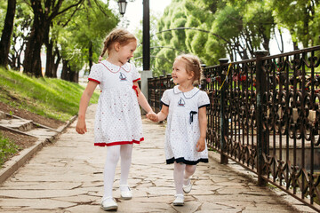 Two blonde European-looking child sisters hold hands and look at each other and smile. The concept of happy family friendship love. Walking in nature in the park laughing and smiling