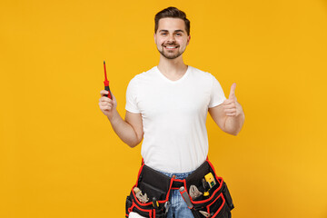 Young smiling excited employee handyman man in white tshirt hold screw instrument tool show thumb up isolated on yellow background Instruments accessories renovation apartment room Repair home concept