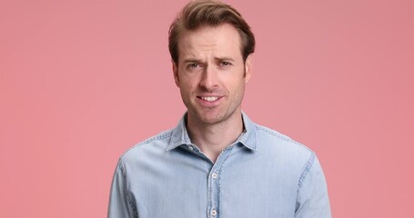 Wall Mural - handsome young fashion model in denim shirt pointing finger to head and military saluting while walking on pink background in studio