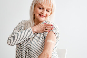 Senior Woman Showing Vaccinated Arm After Antiviral Injection, White Wall