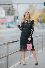 Poster - Blonde female posing in an elegant black evening dress holding a pink bag