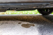 Parked car in driveway with macro closeup of vehicle leaking fuel on cat litter to prevent damaging pavement and to absorb the gas