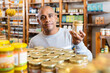 © JackF - Smiling Latin American man choosing foods in supermarket, reading jar contents on label