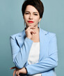 © Dmitry Lobanov - Portrait of short haired brunette businesswoman, analyst in blue business smart casual suit and earrings, holding hand at chin over blue background. Stylish business female wear and fashion concept