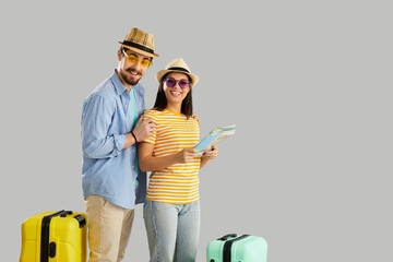 Couple in love holding tourist map standing isolated on blank empty advertising copy space background. Portrait of two happy young people in casual summer wear with travel suitcases ready for vacation