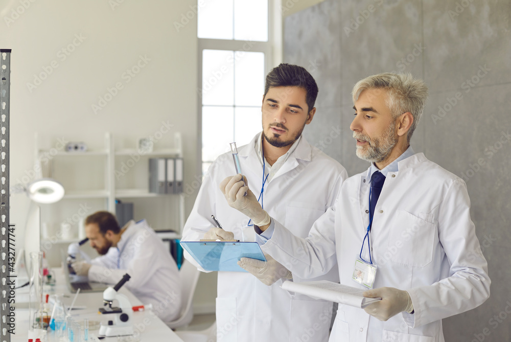 Two scientists in white lab coats and gloves developing new effective ...