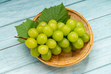 Sweet Green Grape In Bamboo Basket On Wooden Table, Japanese Shine Muscat Grape With Leaves On Blue Wooden Background.