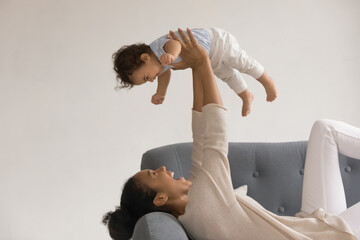Wall Mural - overjoyed young african american mother relaxing on couch play with cute little toddler baby girl ch