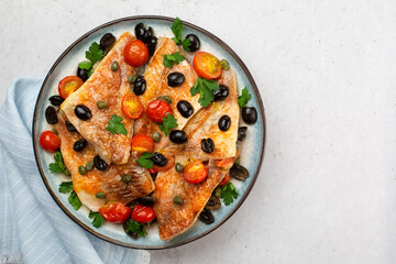 Wall Mural - Perch fish fillets stew, italian style, with black olives, tomatoes and capers, with fresh parsley. On light blue plate. On light grey background. Top view.