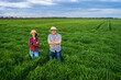 Proud two generations farmers are standing in their barley field in sunset.