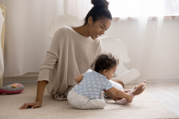 Wall Mural - caring young african american mom sit on floor at home play with little toddler daughter kid. happy 